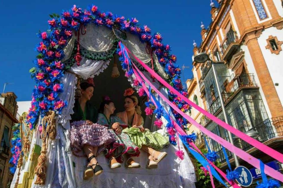 Tres mujeres subidas en una carreta en la salida de la Hermandad de El Rocío de Triana del popular barrio sevillano esta mañana hacia la aldea de El Rocío. JULIO MUÑOZ EFE